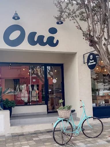Frente del local de Oui en Constitución 1226, con el cartel del wordmark y una bicicleta turquesa apoyada en la vereda